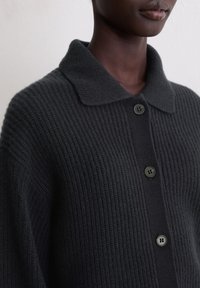 Cardigan en tricot gris foncé avec une texture côtelée, doté d'un col chemise et de quatre boutons ronds noirs sur le devant.