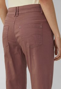 Jasnofioletowe spodnie o gładkiej fakturze, z wysokim stanem, tylnymi kieszeniami z detalami w postaci przeszyć oraz subtelnymi metalowymi akcentami.