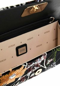 Sac en tissu noir avec broderie florale, quincaillerie dorée et intérieur beige comportant un motif de logo de la marque en répétition et un fermoir sécurisé.