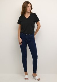 Černé triko s V výstřihem, kombinované s tmavě modrými skinny džíny. Bílé otevřené lodičky na podpatku. Jednoduchý design, hladká látka a přiléhavý střih.