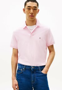 Lichtroze poloshirt met een omgekragen kraag en korte mouwen, voorzien van een klein logo. Gecombineerd met blauwe spijkerbroek met een subtiele textuur.