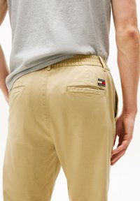 Pantalones caqui con cintura elástica, dos bolsillos traseros y un pequeño parche de logo multicolor de Tommy Jeans en el bolsillo derecho.