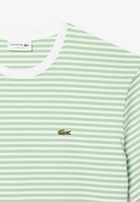 Camiseta de algodón a rayas verdes y blancas con cuello redondo ribeteado y logo de cocodrilo bordado en el lado izquierdo del pecho. Diseño de corte clásico.