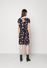 Blommig klänning med marin bakgrund, med korta ärmar, en cutout-detalj på ryggen och rosa blommönster över hela.