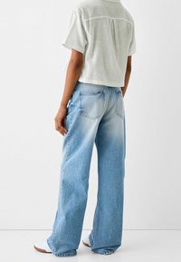 Jasnoniebieskie jeansy o szerokich nogawkach z wyblakłą fakturą, dwoma tylnymi kieszeniami i lekkim przetarciem na krawędziach, zestawione z krótką, białą bluzką z krótkim rękawem.