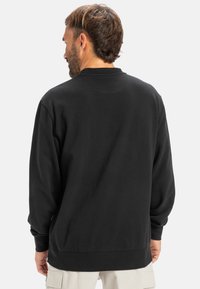 Sudadera negra de manga larga y corte relajado. Presenta un cuello redondo, puños acanalados y una textura suave. Diseño minimalista.