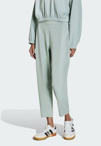 Jasnozielone spodnie dresowe o zwężanym kroju, wykonane z gładkiego materiału, z elastycznym paskiem w talii. Połączone z białymi sneakersami i czarnymi akcentami.