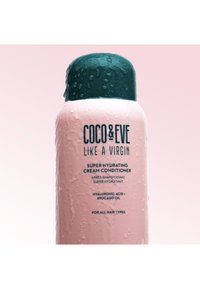 Botella rosa de acondicionador con una tapa verde oscuro, superficie texturizada con gotas de agua, que presenta etiquetas en texto negro detallando los ingredientes.