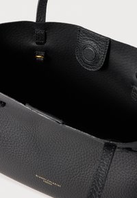 Geantă tote din piele neagră cu textură granuloasă, având un interior spațios, mânere superioare și un accent cu logo auriu pe lateral.