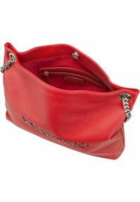 Sac à main en cuir rouge avec un intérieur texturé, des bandoulières en chaîne argentée et un logo à l'avant ; l'intérieur comprend une poche zippée.