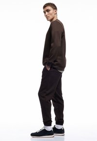Brun sweatshirt med rund hals og ribbede manchetter, parret med matchende sweatpants. Sneakers har en mørk farve med hvide elementer.