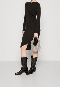 Černé dlouhé šaty s řasením, asymetrickým lemem, doplněné stříbrně zdobenou kabelkou a černými koženými botami na špičku.