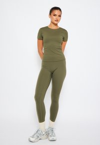 Olivgrön, figursydd träningsskjorta och tights i släta, elastiska material, kombinerat med grå sneakers med ljusa detaljer och krämfärgade strumpor.