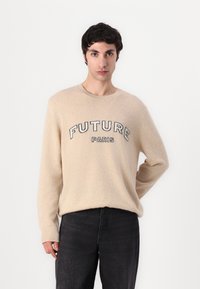 Beige genser laget av mykt materiale med "FUTURE" og "PARIS" i svarte bokstaver over brystet; avslappet passform, rund hals, lange ermer.