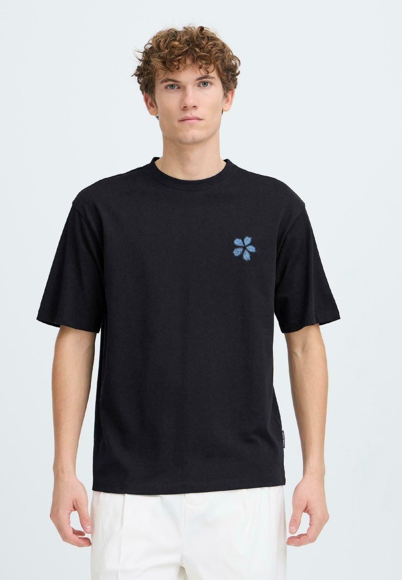 Μαύρο βαμβακερό t-shirt με κοντά μανίκια, που διαθέτει μικρή μπλε κεντημένη λουλουδάτη λεπτομέρεια στο αριστερό μέρος του στήθους. Κανονική γραμμή, άνετη εφαρμογή.