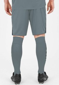 Pantaloni sportivi grigi con una finitura texture e spacchi laterali, abbinati a calze alte fino al ginocchio coordinate e scarpini da calcio neri.