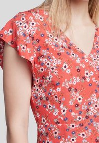 Röd blommig klänning med V-neck, korta volangärmar och åtsittande midja. Har små vita, blå och lila blommor på ett texturerat tyg.