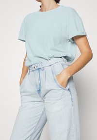 T-shirt in cotone azzurro chiaro con maniche arrotolate, abbinato a jeans in denim chiaro a vita alta con chiusura a bottone e tasche laterali.