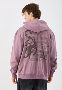 Μωβ φούτερ με μεγάλος γραφικό σχέδιο στην πλάτη που περιλαμβάνει κείμενο και αφηρημένο σχέδιο. Φτιαγμένο από βαμβάκι, με ελαστικές μανσέτες και στρίφωμα.