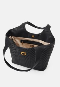 Black quilted tote bag with gold logo accent, two straps, and beige interior featuring compartments. Made of smooth leather material.