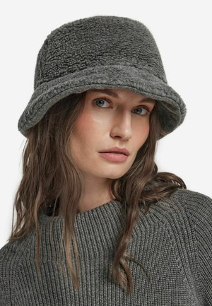 Grå bucket-hatt gjord av mjukt, texturerat material med en bred brätte och sydd kant. Bärs med en matchande ribbad grå tröja.