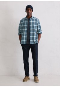 Niebiesko-biała koszula w kratę na guziki, noszona na czarnej koszulce. Dobra do ciemnych spodni i beżowych zamszowych butów. Czapka z dzianiny o fakturze.