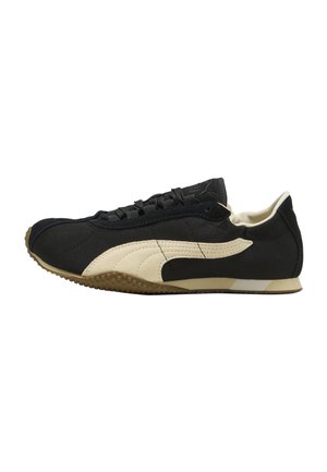 Black and beige low-top sneaker with textured rubber sole and lace-up design, viewed from the side on a white background.