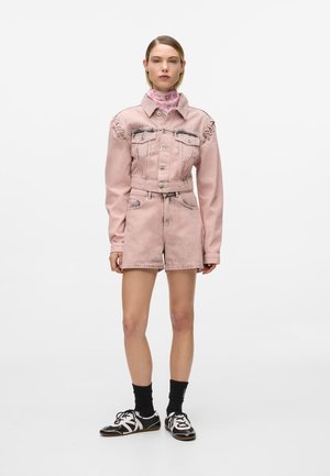 Roosa teksatagi detailse tikkimise ja taskutega, koos sobivate lühikeste pükstega. Välimuse täiustavad mustad ja valged kingad kontrastsete sokkidega.