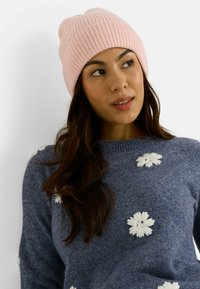 Gorro rosa de canalé con textura suave. Combinado con un suéter azul con bordado floral blanco. Accesorios sencillos y cálidos para el invierno.