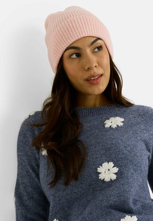 Bonnet rose côtelé avec une texture douce. Associé à un pull bleu orné de broderies florales blanches. Accessoires simples et chauds pour l'hiver.