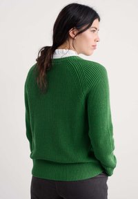 Roheline ribakudumiskampsun ümmarguse kaeluse ja pikkade varrukatega. Tekstuuriga muster üle kogu, vööst kergelt vormitud, valge volangiga särgi kohal.