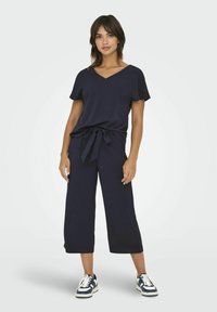 Navy dvoudílný outfit s vrškem s krátkým rukávem a V-výstřihem, který má zavazování v pase, a širokými kalhotami do délky ke kotníkům. Pohodlná textilní struktura.