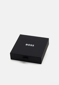 Črni kvadratni škatla s predalnim dizajnom. Na vrhu se nahaja bel odtisnjen logotip "BOSS". Narejena je iz gladkega, mat materiala.