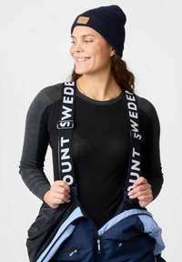 Marine Beanie, schwarzes Langarmshirt und blaue Oberbekleidung mit weißen Riemen, auf denen "MOUNT SWEDEN" steht. Merkmale sind Kontrastnähte und Reißverschlüsse.