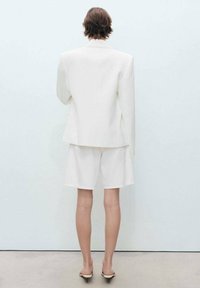 Blazer blanc sur mesure associé à un short assorti, fabriqué dans un tissu lisse. Le blazer présente des épaules structurées et une silhouette épurée.