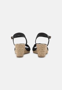 Sandales compensées noires avec des brides à la cheville, dotées d'un talon texturé en forme de corde, d'un dos ouvert et d'un dessus en matériau lisse.