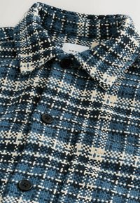 Blue and black plaid shirt with a textured weave, two black buttons, and a pointed collar. Label reads "NEXT" inside the collar.