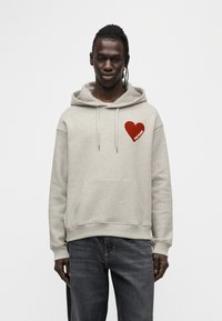 Sweat à capuche gris en tissu doux avec un grand motif rouge en forme de cœur et le mot "FUTURE" en blanc. Poche kangourou à l'avant.