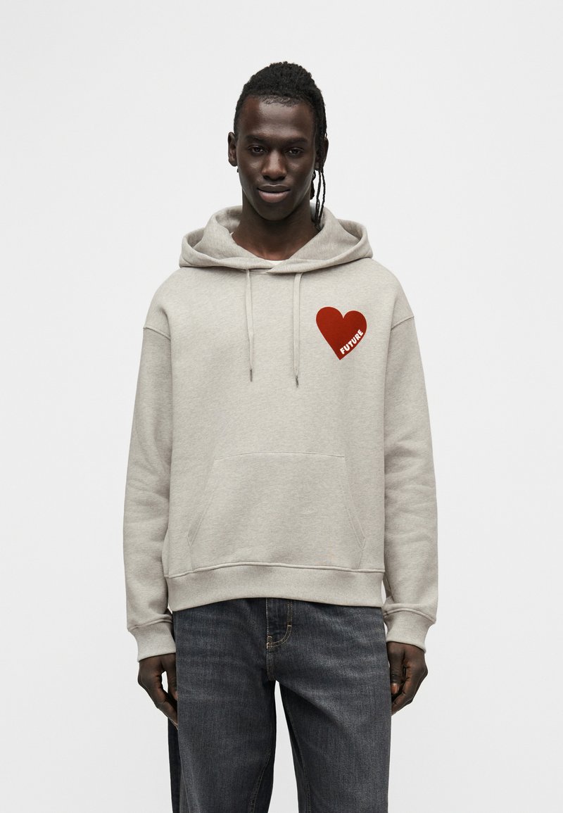 Sweat à capuche gris en tissu doux avec un grand motif rouge en forme de cœur et le mot "FUTURE" en blanc. Poche kangourou à l'avant.