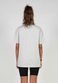 Lys grå, oversized bomull t-skjorte med korte ermer og rund hals, sett fra baksiden, kombinert med sorte shorts.