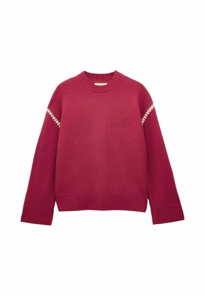 Sarkana svītrainā džemperis ar ribotu apkakli, garām piedurknēm, baltām zigzaga šuvēm pie plecu šuvēm, kā arī ribotām piedurknēm un apakšdaļu.