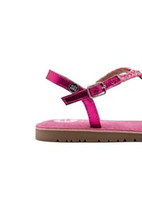 Sandalia metálica rosa con tiras trenzadas, detalle de hebilla, plantilla suave en rosa y suela marrón texturizada con surcos para mayor tracción.
