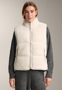 Hellbeige Fleeceweste mit hohem Kragen, Reißverschluss vorne und Reißverschlusstaschen. Die Weste ist gesteppte und erzeugt so eine strukturierte Optik.
