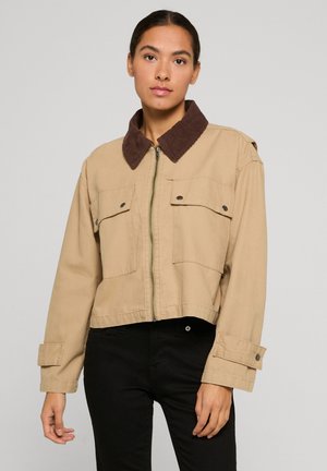 Giacca beige tagliata con colletto in velluto a coste marrone, due tasche frontali con pattina e chiusura con cerniera. Presenta maniche con polsini e tessuto resistente.