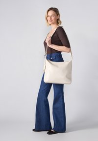 Beige woven leather shoulder bag with a curved shape, adjustable strap, and gold-tone hardware, displayed against a light background.