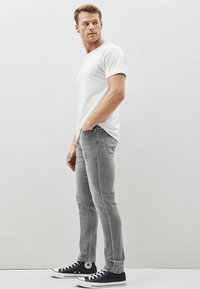 Jeans grii tip slim-fit, din amestec de bumbac, cu cinci buzunare, asortați cu un tricou alb simplu și teniși negri cu talpă joasă și accente albe.