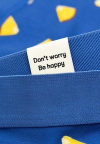 Clothing label on blue fabric with yellow shapes reads "Don't worry Be happy" in black text.