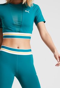 Teal atletisk crop top med korta ärmar, med en meshpanel. Teal högmidjade leggings med en randig midja i blått, gult och vitt.