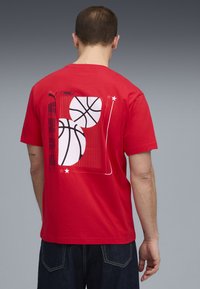 Rød bomulds T-shirt med et grafik af to basketballer og lodrette linjer på ryggen. Rund halsudskæring, korte ærmer, afslappet pasform.
