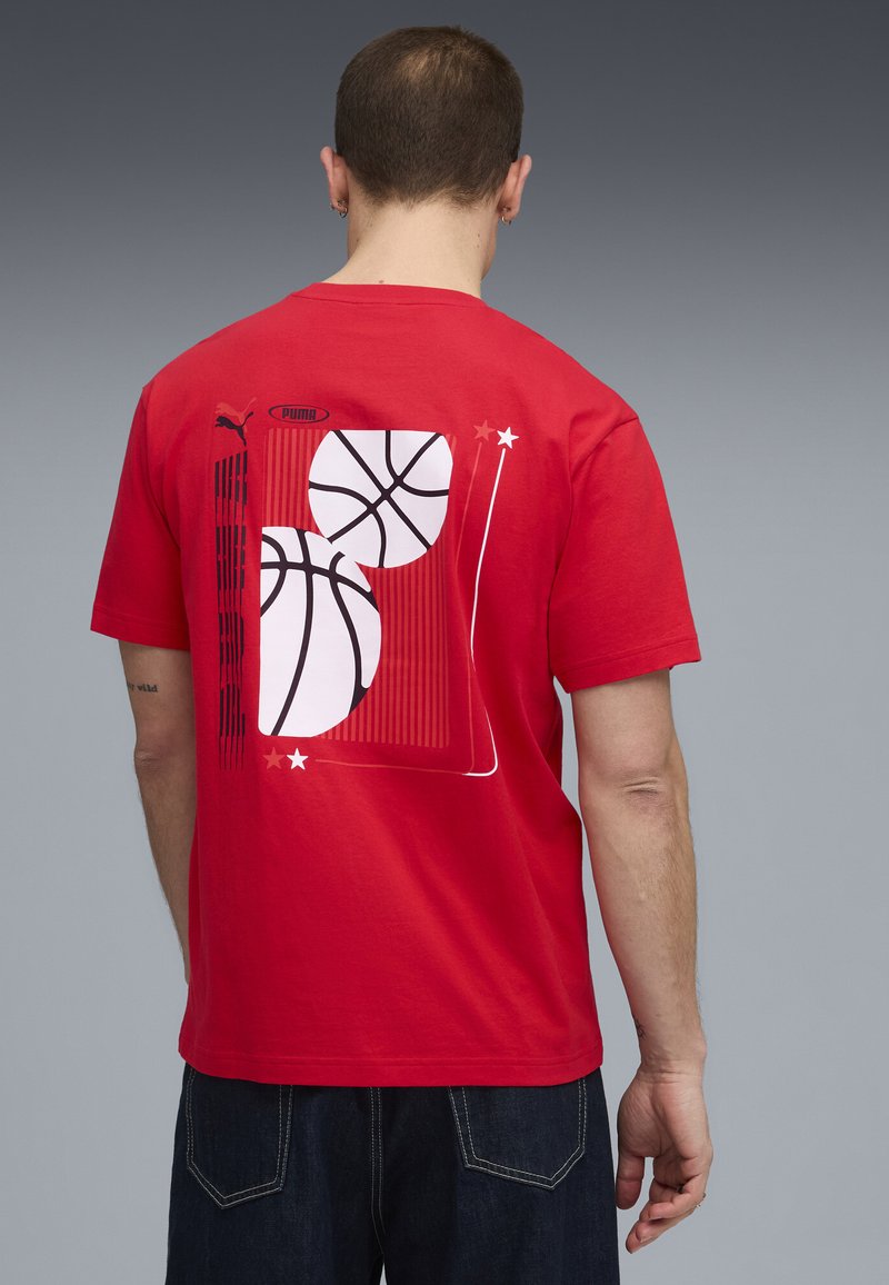 Rød bomulds T-shirt med et grafik af to basketballer og lodrette linjer på ryggen. Rund halsudskæring, korte ærmer, afslappet pasform.